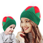 Parent and child in matching green and red Christmas knit beanies, smiling together"