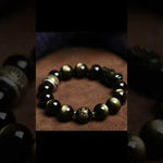 Gold obsidian bracelet with natural black and gold gemstone beads and traditional decorative design on white background

